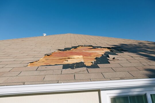 Damaged roof shingles exposing splintered plywood decking and underlay after a storm, featuring gritty textures for roofing repair and insurance claims