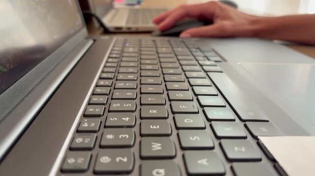 A person's hands typing on a modern laptop keyboard. The action of writing, coding, or working on a computer in a well-lit environment