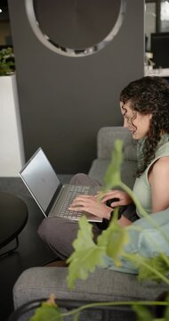 Vertical video: African American woman after sitting on office sofa, typing on laptop while working
