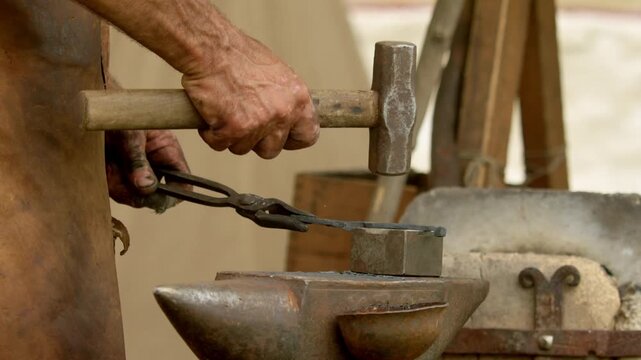 Close macro perspective focuses on impact of hammer face on workpiece, metal scale dust, and weathered texture of anvil top in outdoor forge.