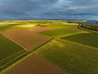Obraz premium High angle wide horizontal aerial drone photograph of polder fields, drainage canals, Lake Veere, and storm sky in Kamperland, Zeeland, Netherlands in golden hour summer sunlight