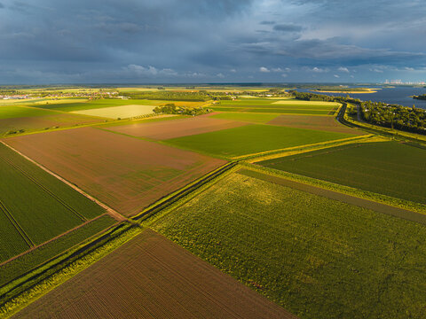 High angle wide horizontal aerial drone photograph of polder fields, drainage canals, Lake Veere, and storm sky in Kamperland, Zeeland, Netherlands in golden hour summer sunlight