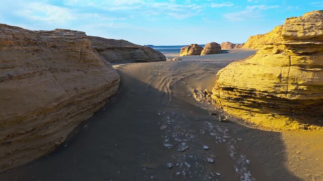Eroded sandstone yardangs and layered cliffs frame a sandy desert passage in Dahaidao, Hami, China, ideal for geology, adventure travel and nature backgrounds.