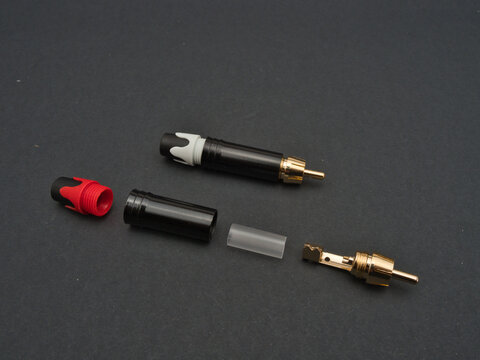 RCA Phono Plugs and Components - Disassembled RCA phono plugs with golden connectors and black, red, white, and clear housing components on a dark background.