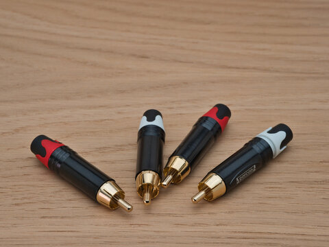 RCA Connectors on Wood - Four black and gold-plated RCA phono plug connectors with red and white accents lying on a natural wooden surface.