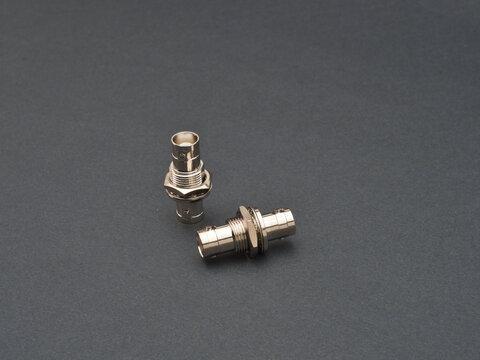 Two Metallic BNC Connectors - Two shiny silver BNC (Bayonet Neill-Concelman) connectors are displayed against a dark gray background, one standing upright and the other l