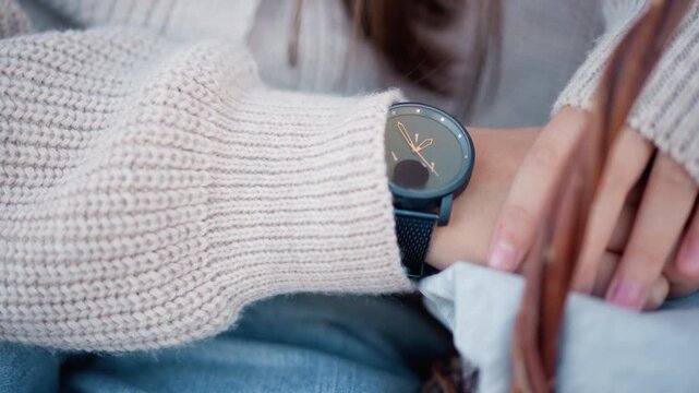 Close up of woman wearing blue watch on wrist with beige knit sweater and denim jeans resting hands near wicker basket with folded fabric soft lighting