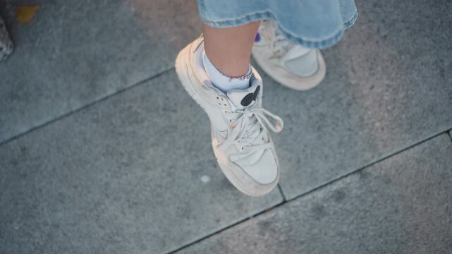 Close up of young woman feet in white sneakers and light blue jeans walking on gray pavement. focus remains steady capturing movement from various angles with consistent lighting throughout