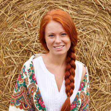 A portrait of a young village woman in a white blouse and with a scarf on her shoulders.