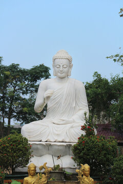 White marble Buddha statue meditating on lotus throne with Vitarka Mudra gesture, outdoor religious monument in temple garden, Hue, Vietnam