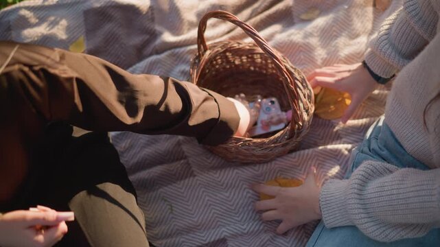 Close up of two people adult and child interacting with objects on soft fabric. woman reaches into wicker basket while holding leaves both subjects engage in gentle hand movements