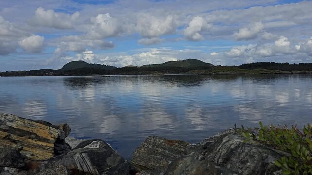 Large granite rocks dominate the foreground, while a dark forested shoreline with rolling hills stretches into the distance. Norway, Toska. September
