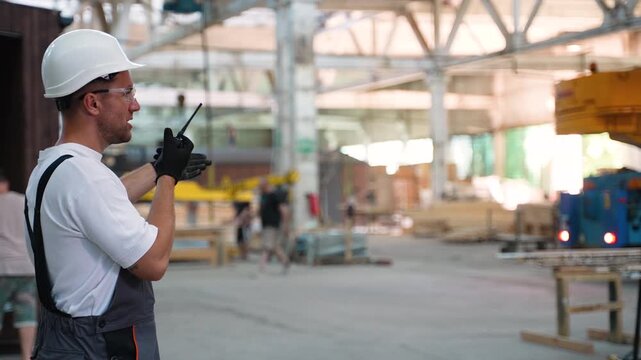Factory worker coordinating crane operation with walkie talkie