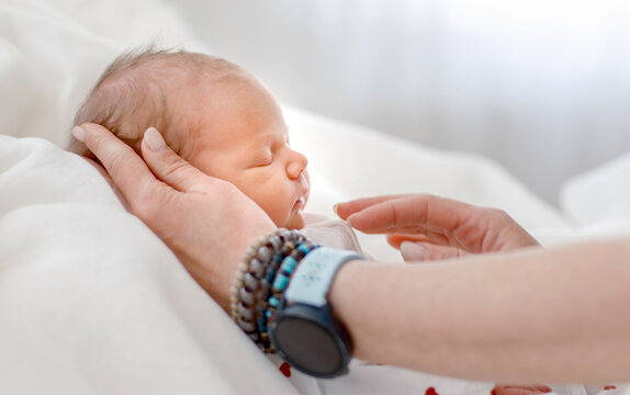 Hands cradle sleeping infant face on soft white fabric background during daylight studio session