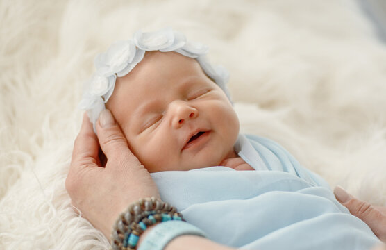 Soft hands holding peaceful infant wearing white flower headband in bright studio morning light