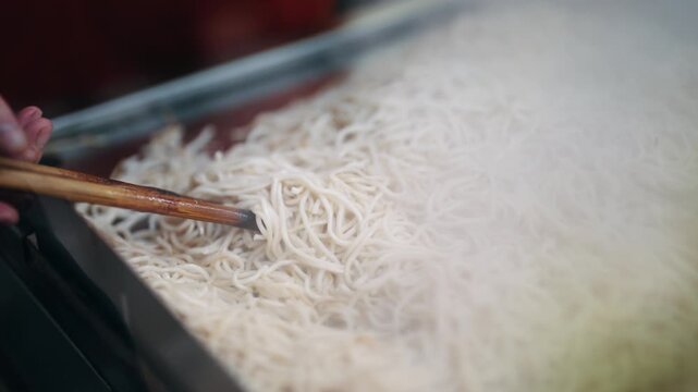 Steaming noodles are stirred with their rich texture and vibrant warmth in chinese restaurant, slow motion