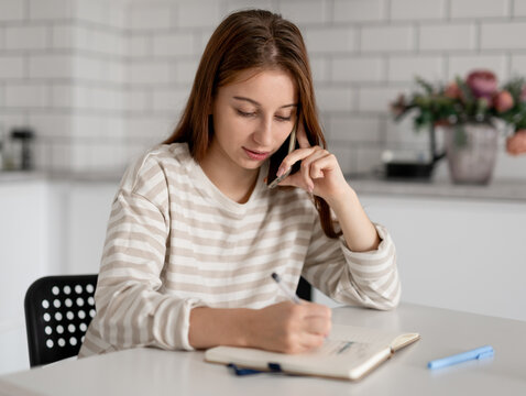 Girl Talks On Phone And Writes In Notebook At Home