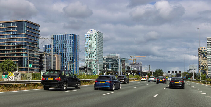 Amsterdam, Netherlands. 22 August 2026. View from the A10 highway with moving cars passing by the modern architecture and skyscrapers of the Zuidas business district.