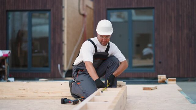 Construction worker measuring wood frame at building site