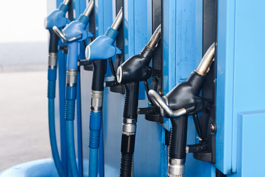 Blue and black fuel pump nozzles hang in holders at a filling station. Multiple gasoline and diesel dispensers with flexible hoses stand ready for cars and vehicle refueling background.