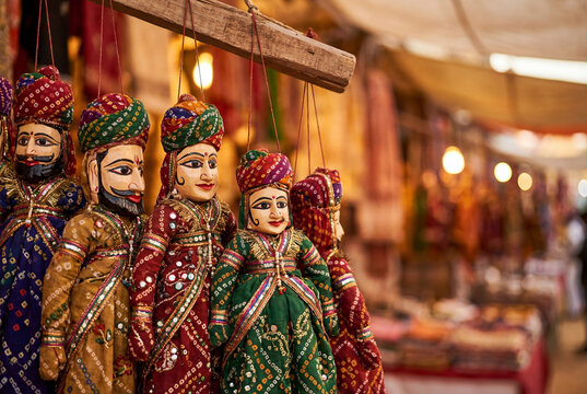 Traditional Rajasthani Kathputli string puppets with colorful Bandhani costumes, turbans and ornate details hanging in an Indian bazaar, showcasing Rajasthan folk art and craftsmanship