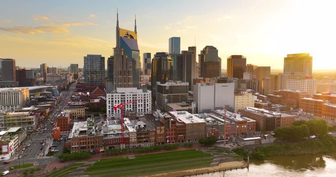 Drone shot of Nashville, Tennessee in evening time. Urban layout with high buildings, waterfront riverbank and bridge over Cumberland river.
