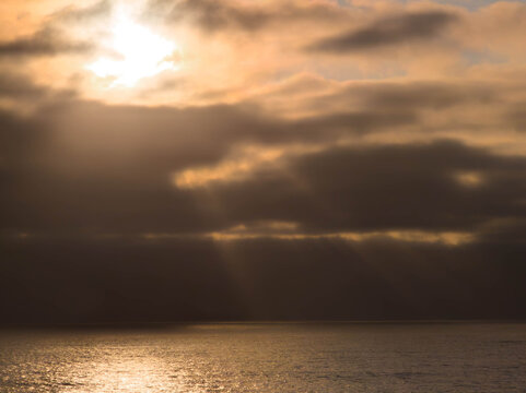 Moody sunset over the ocean with dramatic sunbeams piercing through dark, heavy clouds and illuminating the water along the Oregon Coast.