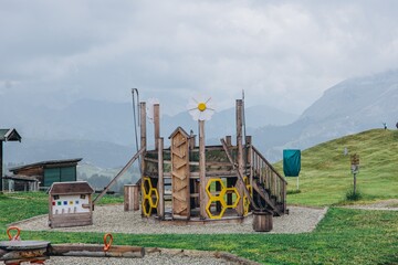 Wooden adventure playground with climbing frames and gears stands on a grassy alpine meadow. Family mountain resort activities and outdoor play for tourism, travel and childrens leisure marketing © Екатерина Лукашина