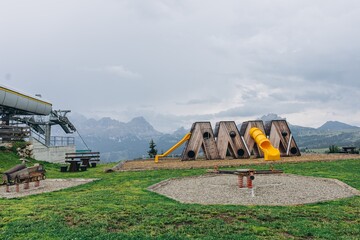 Wide mountain playground with wooden slides, a sandpit and a chairlift base on a green plateau. Alpine summer resort and family mountain tourism for travel, holiday and destination marketing © Екатерина Лукашина