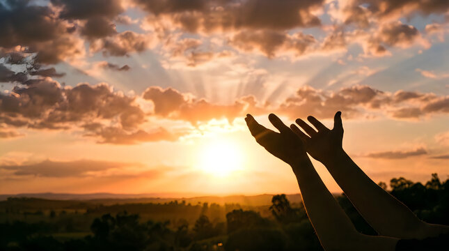 Silhouette of hands raised toward a sunset sky with god rays
