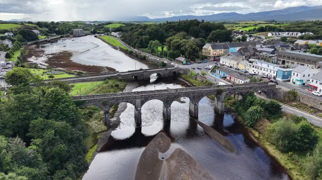 Drone aerial view of Newport, County Mayo, Ireland, featuring the historic Seven Arches Railway Viaduct crossing the Black Oak River. The scene shows the tidal river, stone bridges, colorful town