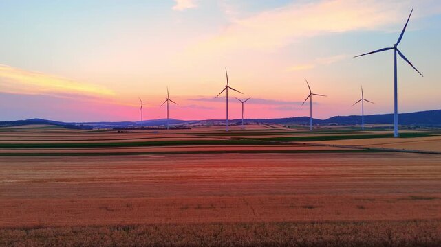 Twilight over agricultural fields and wind turbines. Wide drone shot of rural landscape with sustainable energy generators at dusk.