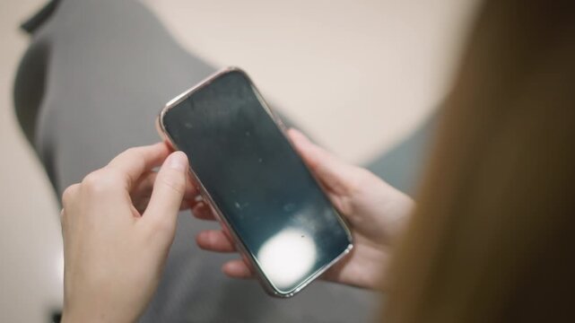 Close up of woman holding and interacting with smartphone in her hands. device is held steadily showing its screen reflecting light while woman manipulates it gently. Soft lighting creates