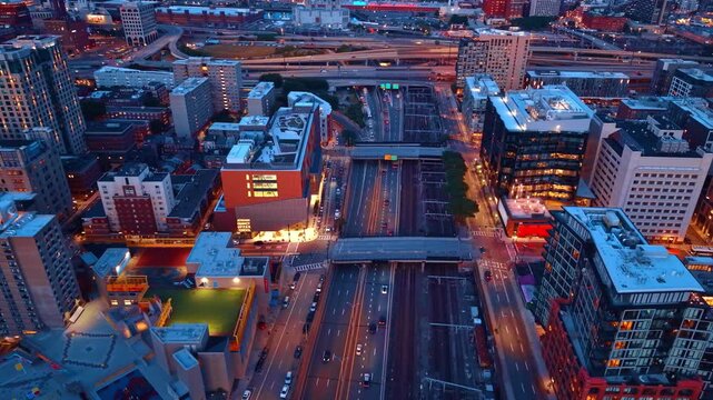 Flying over the multi-lane highway with bridges across it. Beautiful illumination of modern Boston, Massachusetts, USA at dusk time from drone.