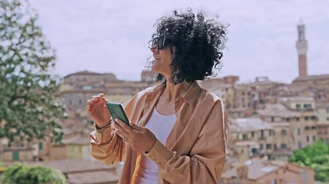 Woman sightseeing historical Siena city while holding a smartphone in Tuscany, Italy