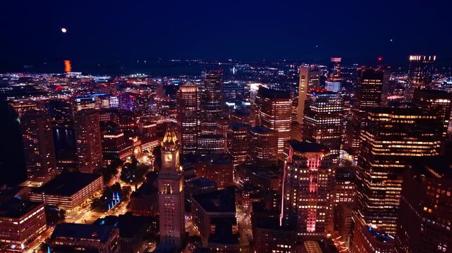 Numerous high-rise buildings with the lights on inside in the beautiful urban landscape of the city downtown. Drone footage above well-illuminated Boston, Massachusetts, USA at night.
