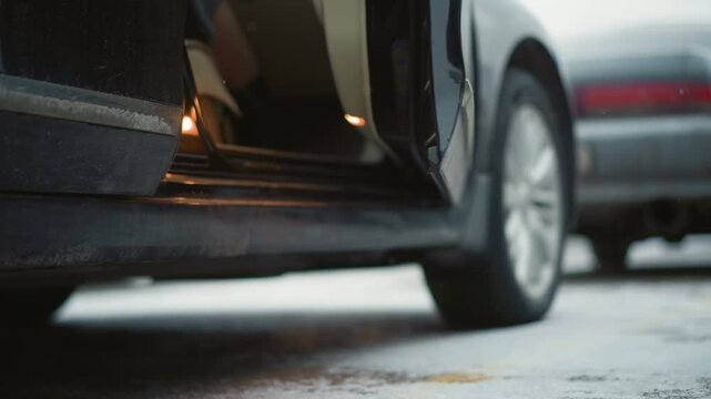 Close up of woman entering rear passenger side of dark colored car. camera focuses on her legs and black patent boots as woman steps into vehicle with soft lighting highlighting texture