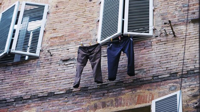 Washed laundry dries on a clothesline strung between windows of a brick facade in Italy