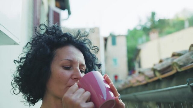 Woman enjoying morning coffee standing on a terrace overlooking the charming rooftops and countryside of Tuscany, Italy
