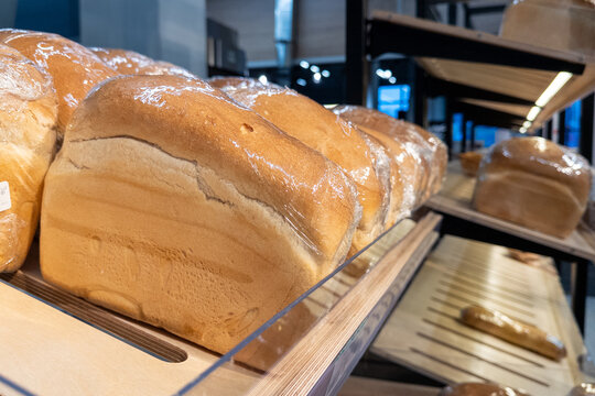Freshly baked loaves of white bread wrapped in plastic film on wooden store shelves