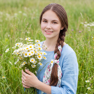 Rustic portrait of a young blonde girl with a bouquet of chamomile in a field