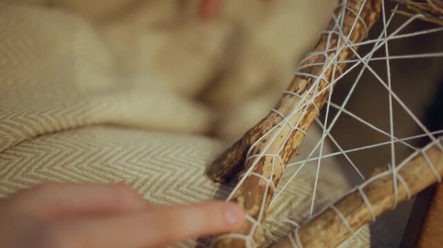 Close up of hand weaving white string around wooden sticks to create intricate pattern on fabric. scene features soft lighting and detailed texture with focus remaining steady throughout