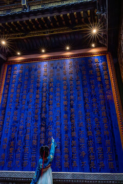 "Woman in Traditional Dress Reading Buddhist Sutra Wall, Temple Interior" / "Mujer con vestimenta tradicional ante muro con el Sutra del Coraz&oacute;n"