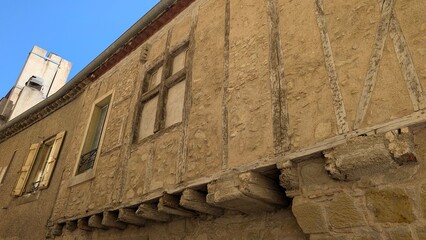 Low-angle view of a medieval house in Carcasonne,  a French old town: a projecting upper floor carried on carved stone corbels, oak timber framing filled with rubble stone, a mullioned window and pale © Beautiful talkers