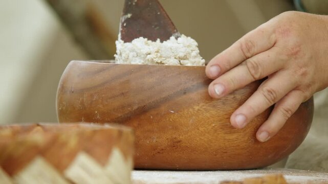 Close up baker mixing flour in wooden bowl while preparing dough during. Traditional hand preparation demonstrates historic breadmaking technique preserved through centuries of rural culinary heritage