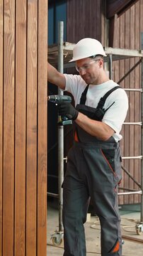 Construction worker using power drill on wooden wall