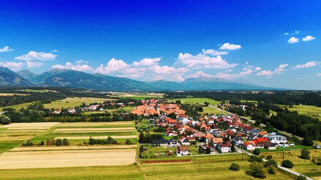 Rural town and farmland near mountain peaks. Striped agricultural fields border a village under a clear blue sky.