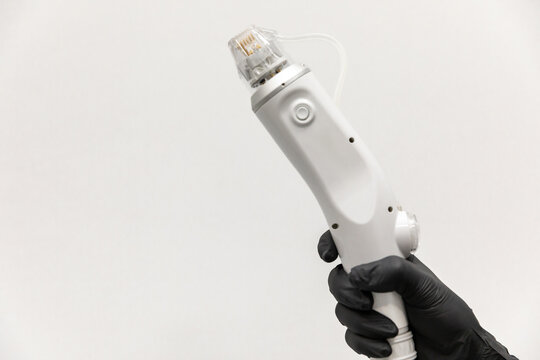 Close up hand in black glove holds white RF microneedling handles device with tip for aesthetic body treatments and skincare procedures on white background. Copy space. Concept of beauty, health