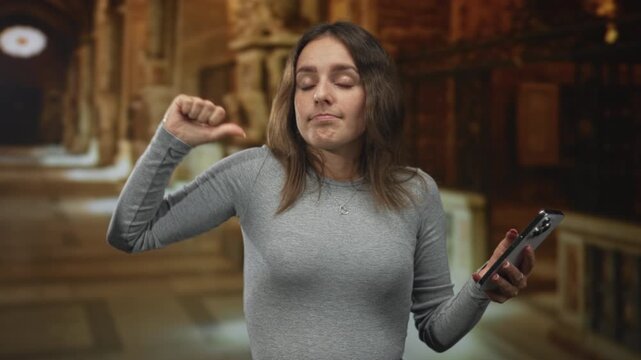 Woman thumb pointing to self while holding smartphone inside a church building, slight shrug and unimpressed expression; indifference dismissal.