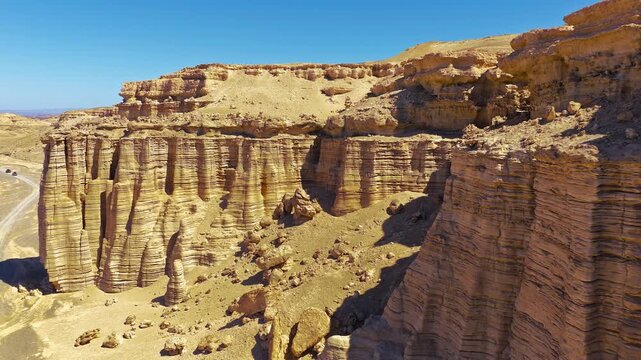 Aerial view of layered sandstone cliffs and eroded canyon formations in a dry desert landscape, ideal for geology, travel, nature and adventure concepts.